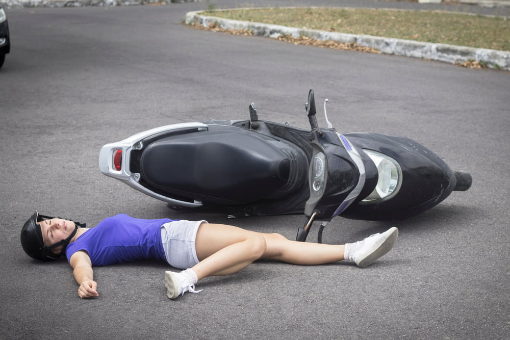 injured moped driver laying on ground next to moped on side after accident