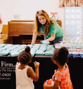 a Jebaily Law Firm team member hands out antibacterial wipes to two young children during a back to school event giveaway