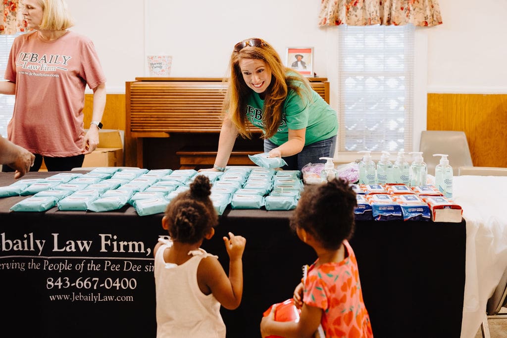 a Jebaily Law Firm team member hands out antibacterial wipes to two young children during a back to school event giveaway