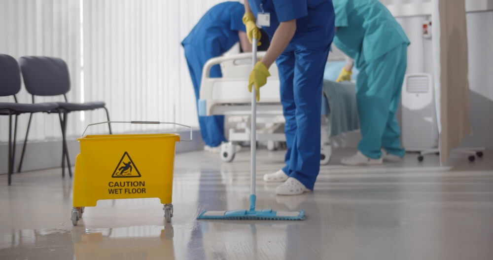 Medical staff in uniform wiping floor and cleaning intensive care unit in modern clinic.