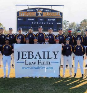 a men's baseball team stands posing on a field for a photo behind a sign reading JEBAILY Law Firm