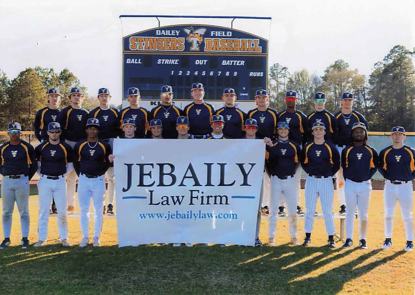 a men's baseball team stands posing on a field for a photo behind a sign reading JEBAILY Law Firm