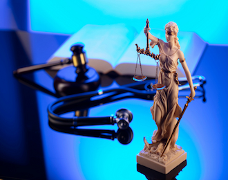 A statue of Lady Justice sitting on a desk, accompanied by a stethoscope. Symbolizing fairness and the intersection of law and medicine.