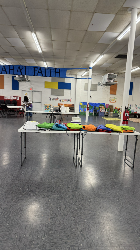assortment of multi colored backpacks laid out on folding table in the center of a room