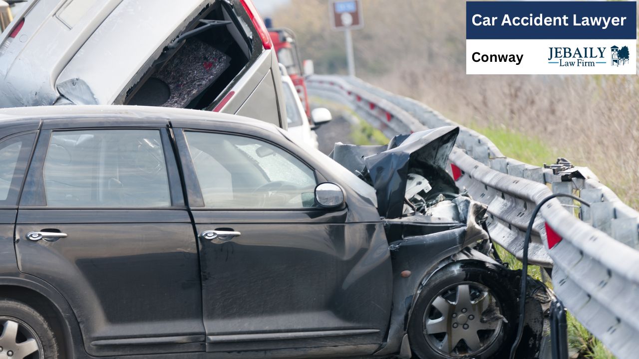 A dark gray/black car is heavily damaged, with its front end significantly dented and crumpled, the hood open, and parts of the interior visible.