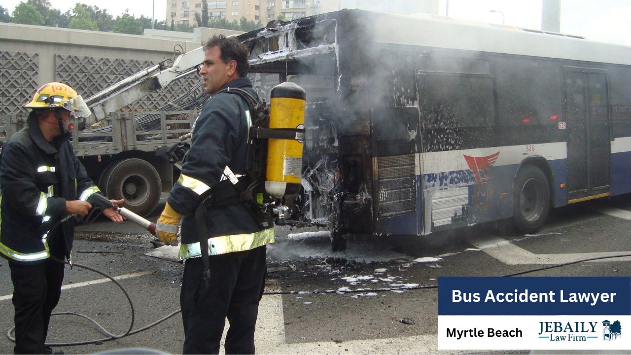 Two firefighters are tending to a severely fire-damaged bus, which is emitting smoke and foam, at what appears to be a road accident scene.
