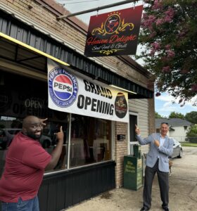 Paul Woodberry and George Jebaily stand under and point to the Grand Opening sign on the exterior of Paul's new restaurant Heaven Delight Soul Food & Grill