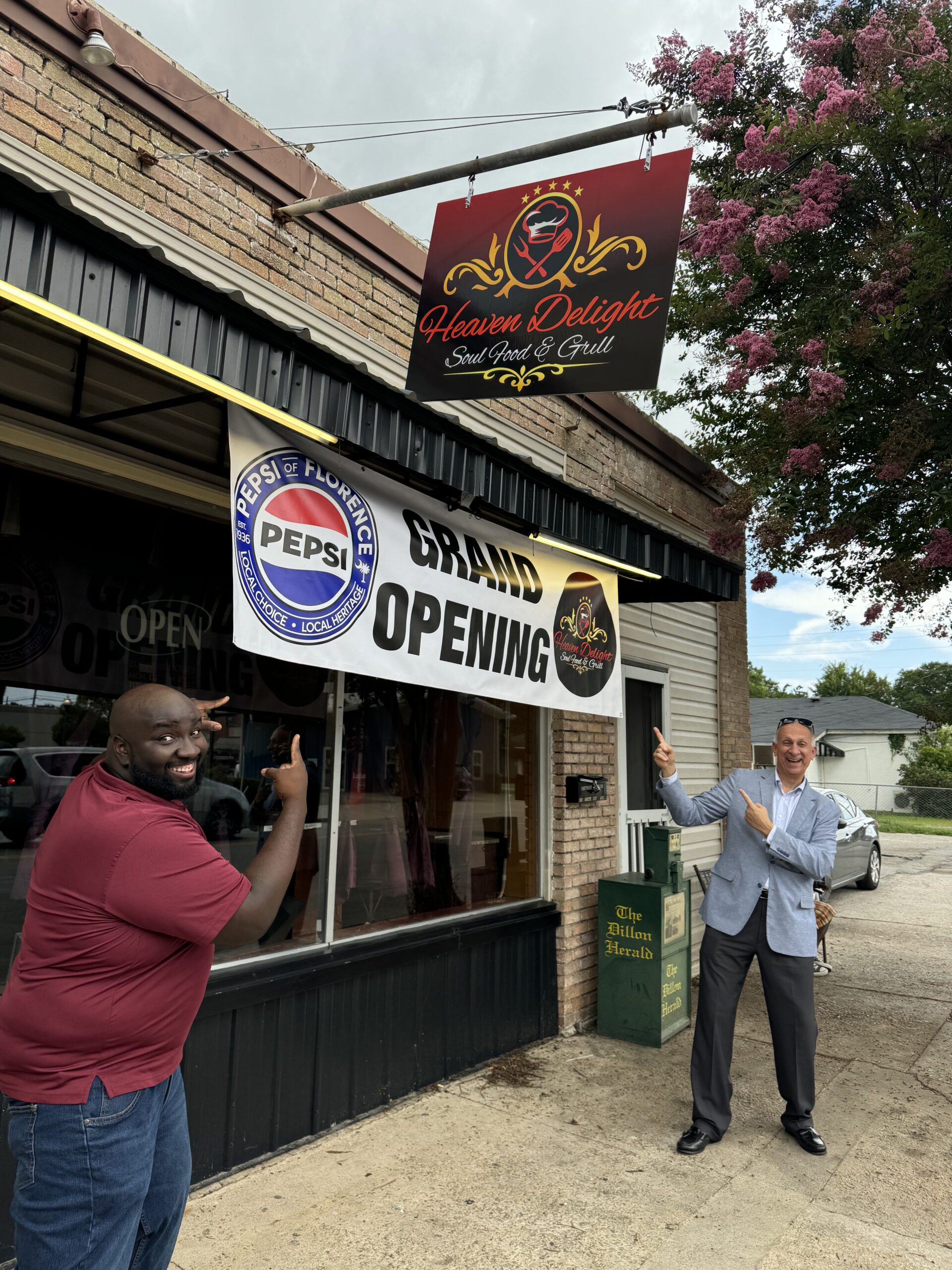 Paul Woodberry and George Jebaily stand under and point to the Grand Opening sign on the exterior of Paul's new restaurant Heaven Delight Soul Food & Grill