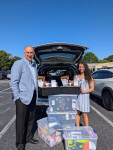 George Jebaily and Kayla Jebaily Adams stand outside posing next to donation of clothing, shoes, and other items for school children