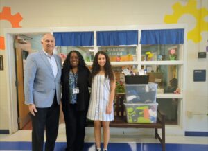 George Jebaily and Kayla Jebaily Adams standing next to donation items and admin representative from Carver Elementary