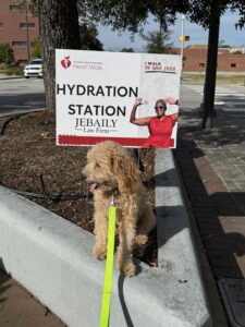 light brown dog sits in front of Pee Dee Heart Walk Hydration Station sign