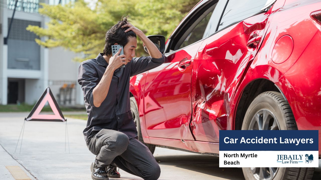 A man is on the phone, looking distressed next to a damaged red car.