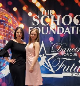 Two people standing in front of The School Foundation event banner in formal wear.