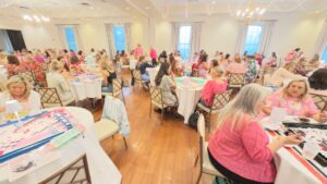 Groups of women sit at tables in a large even room playing Mahjong.